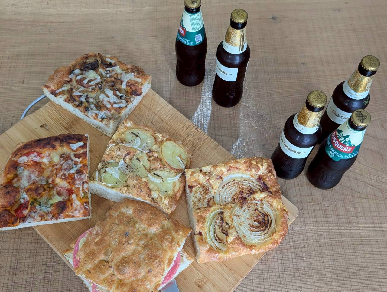 Angled top-down view of focaccia squares and craft beer bottles on a wooden board — Focaccino Hakuba