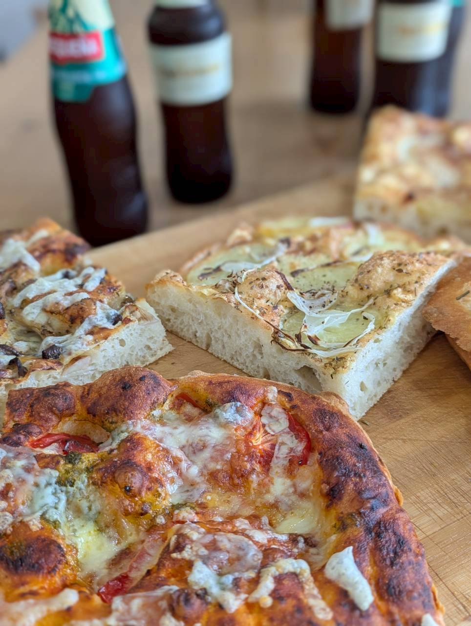 Assorted focaccia slices on a wooden board — margherita, potato and mushroom — with craft beers behind — Focaccino Hakuba