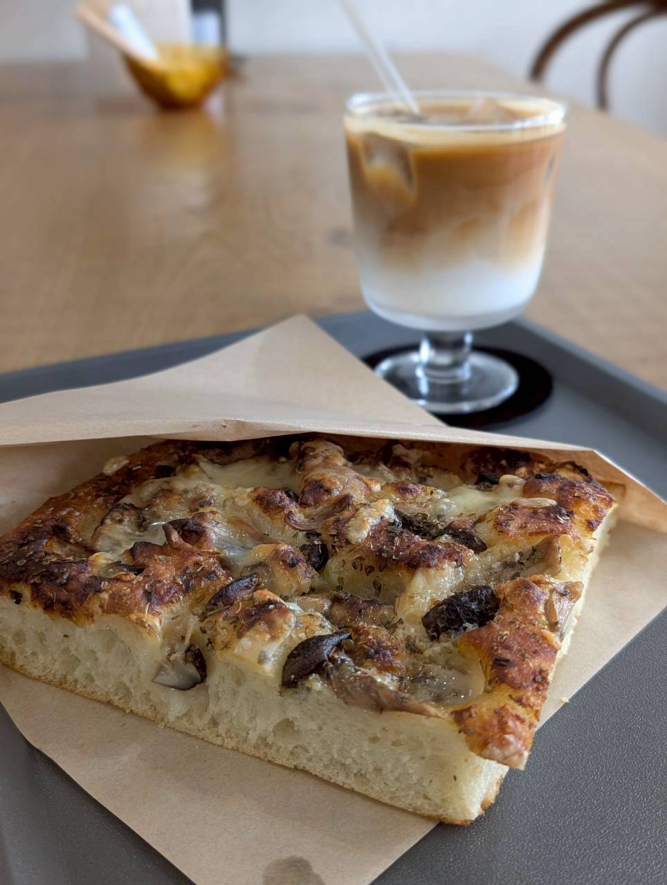 Mushroom and cheese focaccia in a parchment sleeve served beside an iced latte — Focaccino Hakuba Station
