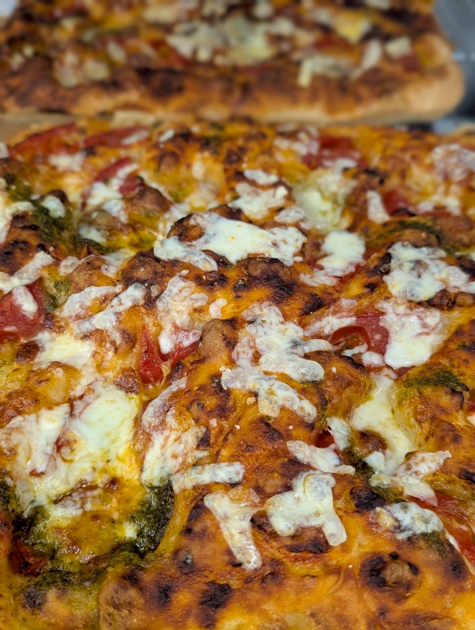 Close-up of pesto and tomato focaccia with bubbling melted cheese and golden charred edges — Focaccino Hakuba