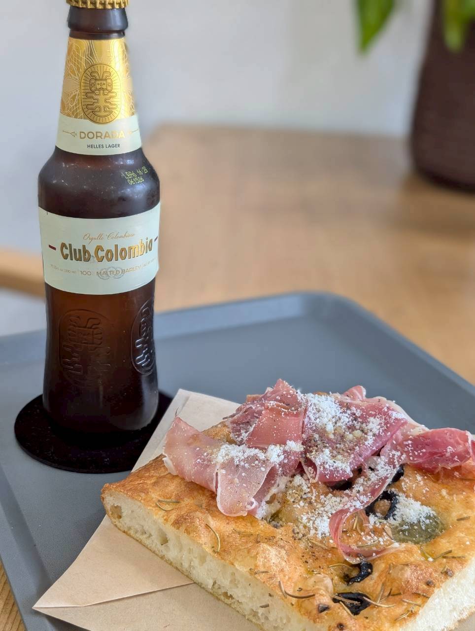Prosciutto focaccia topped with parmigiano and olives, paired with a Club Colombia beer — Focaccino Hakuba