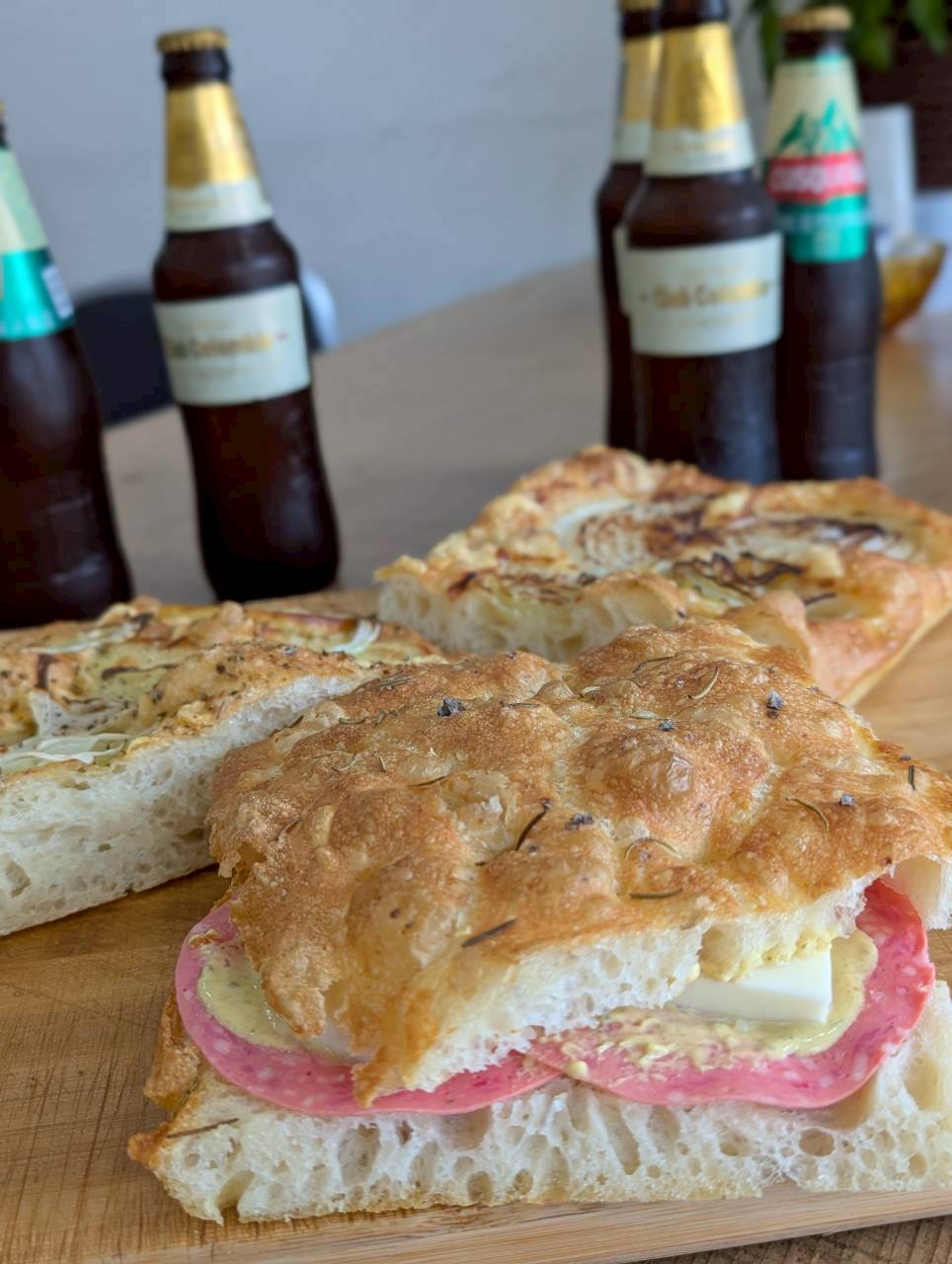 Salami and cheese focaccia sandwich sliced open, served with Colombian craft beers on a wooden board — Focaccino Hakuba