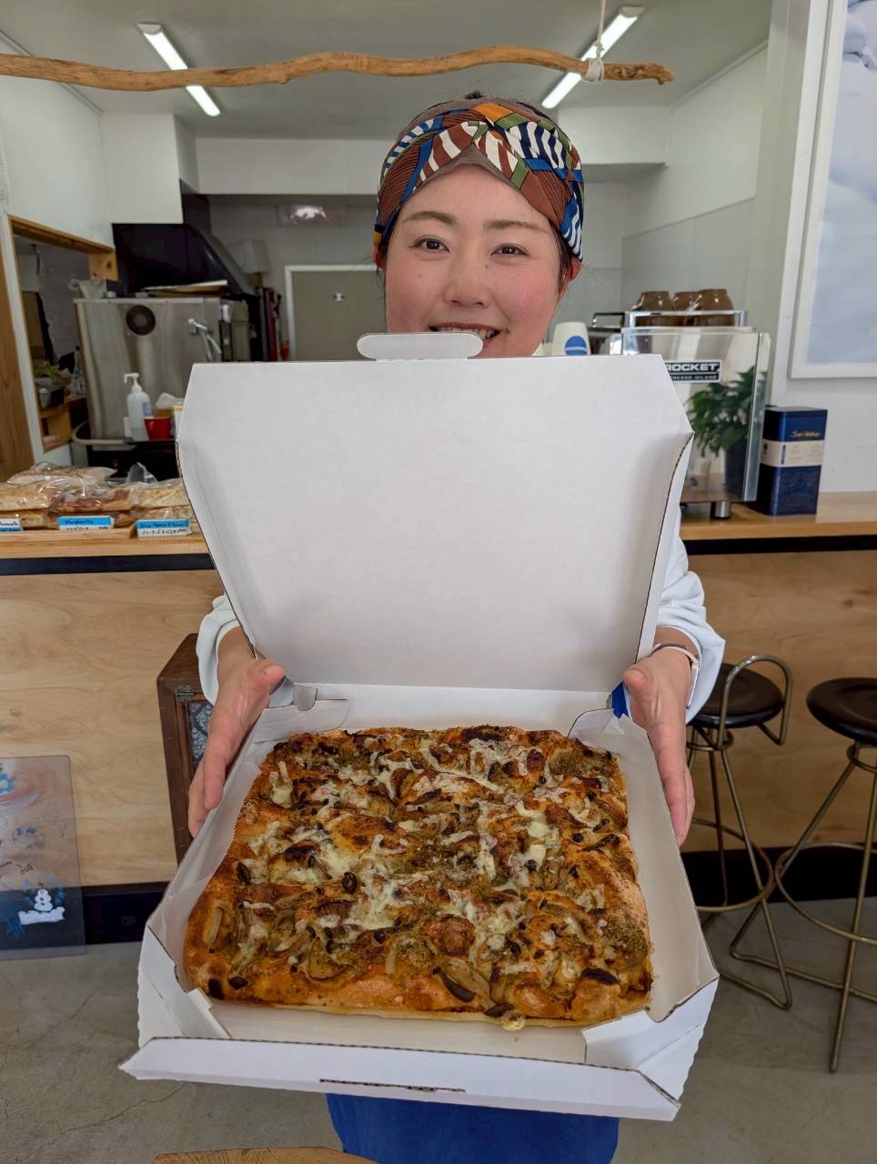 Smiling staff member holding open a takeaway box with a freshly baked square mushroom focaccia inside the cafe — Focaccino Hakuba