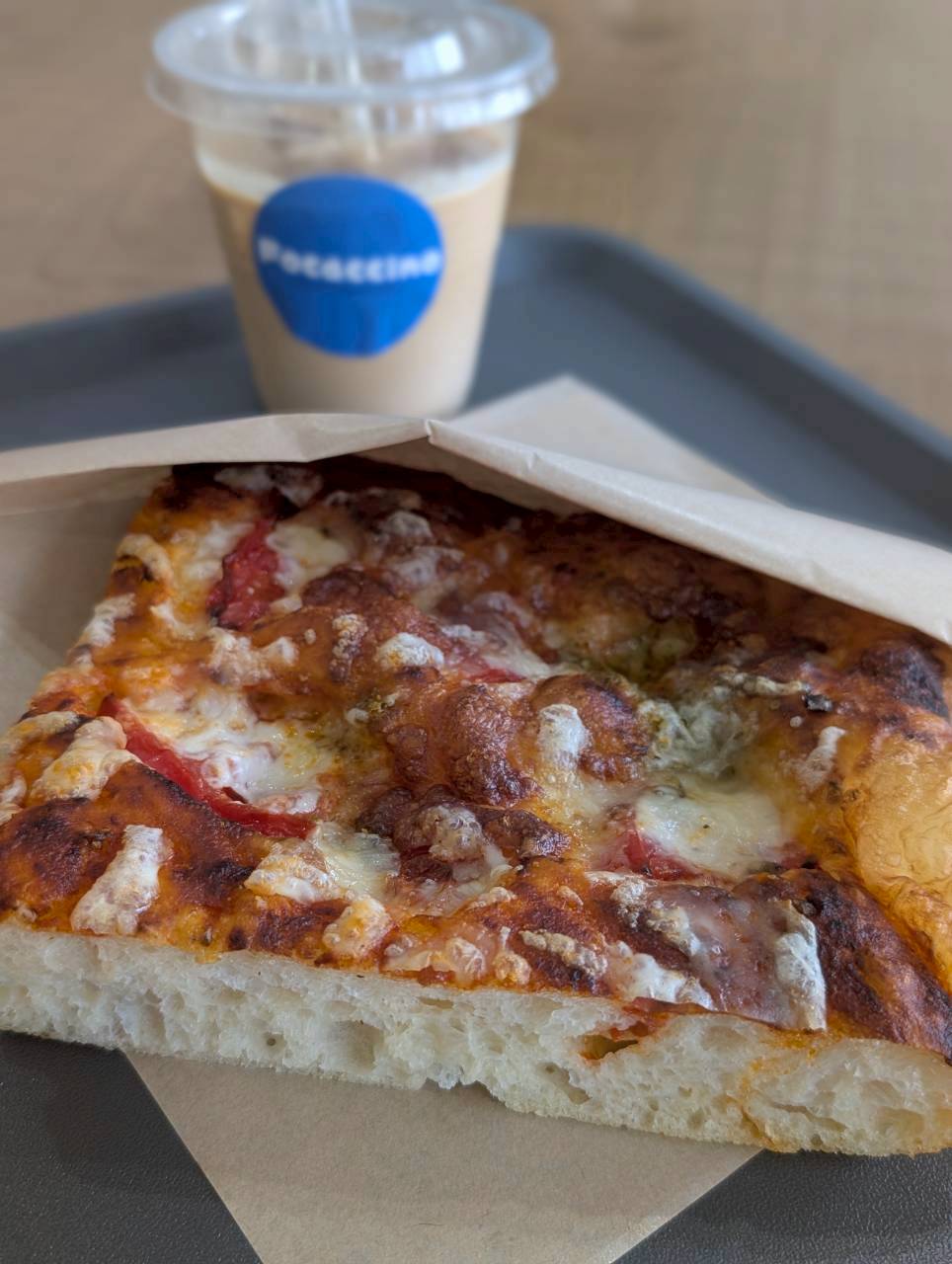 Tomato and cheese pizza-style focaccia slice on parchment next to a Focaccino iced latte — Focaccino Hakuba Station